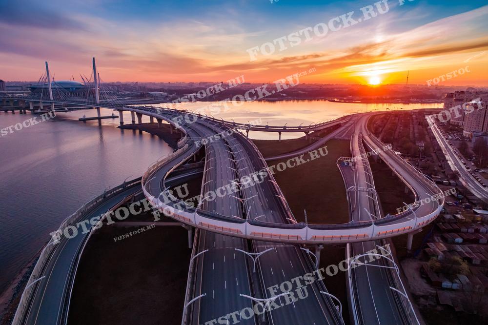 Эта фотография показывает завораживающий рассвет над Санкт-Петербургом с видом на сложную развязку мостов и дорог. Золотые оттенки утреннего неба и отражения в водах Невы делают этот кадр по-настоящему впечатляющим. Такая фотография будет хороша для иллюстрирования статей о городском планировании, инженерном искусстве, а также в качестве декора для современных интерьеров.